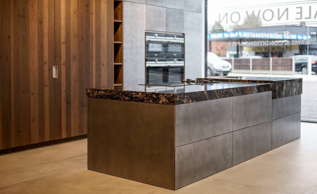 Kitchen island display with a stepped dark stone worktop and metallic-finish units